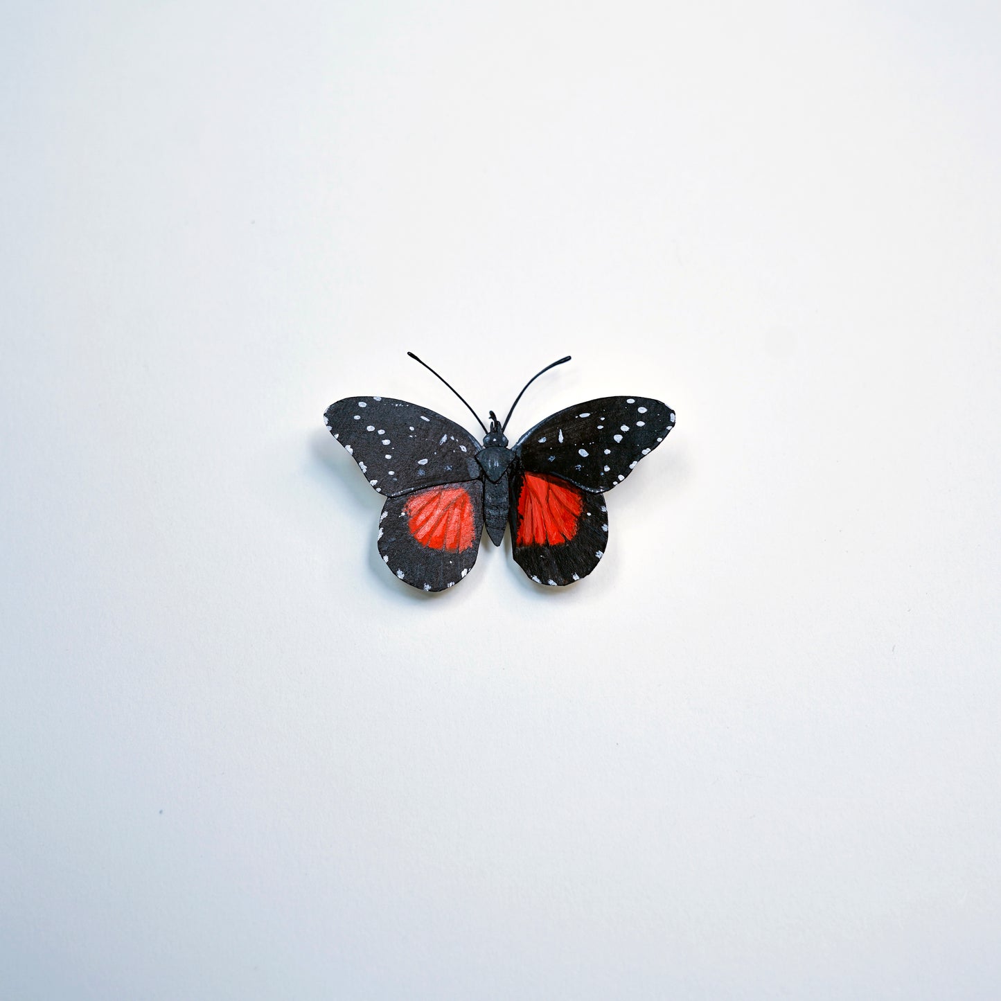 A butterfly art sculpture with black wings speckled with white dots and vibrant red patches on the hindwings, centered on a plain white background.