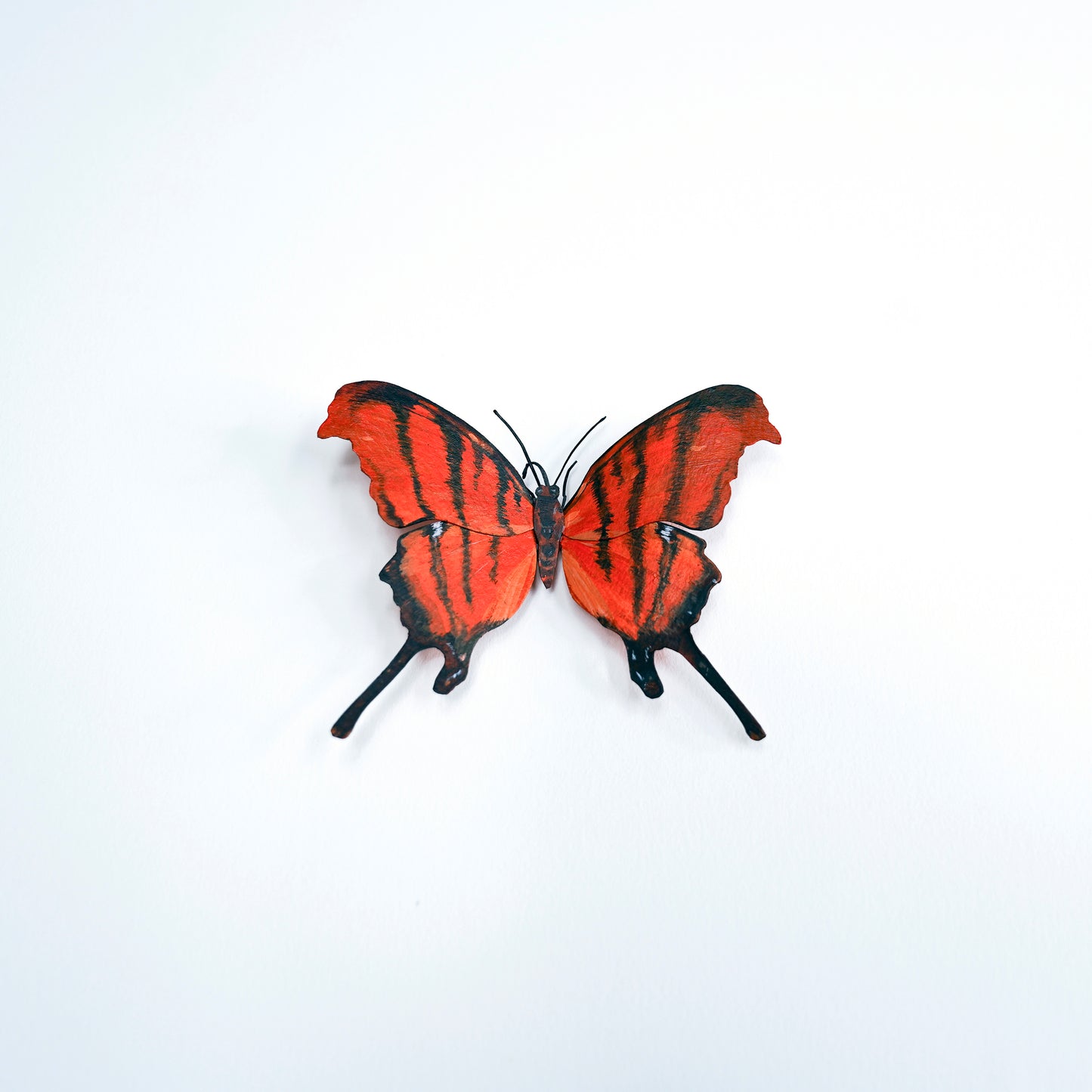 A butterfly art sculpture with bright red-orange wings and bold black stripes, displayed against a plain white background.