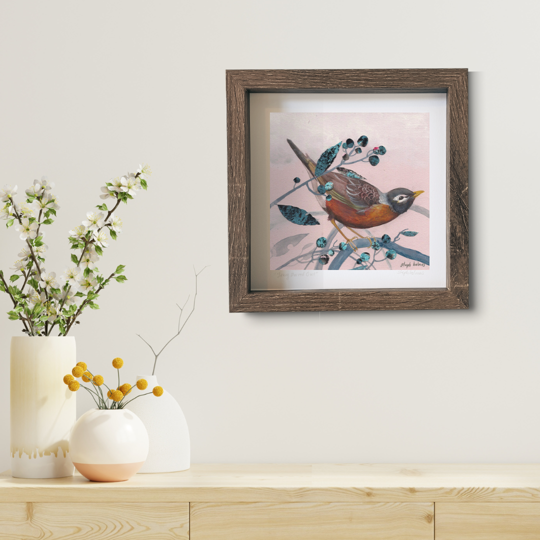 An art print featuring an American Robin in a brown frame above a wooden desk.