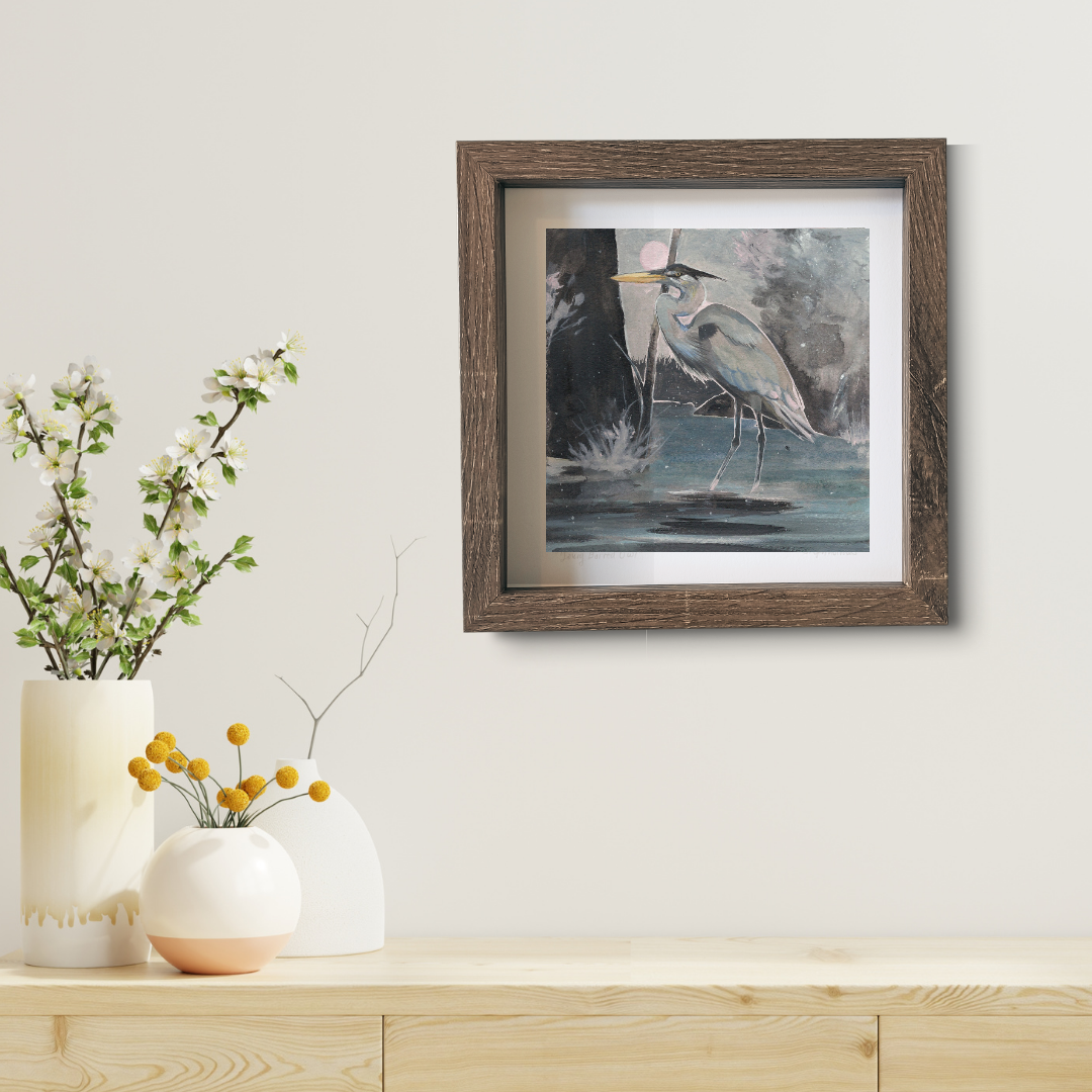 An art print featuring a great blue heron standing in water in a brown frame in a modern living room.