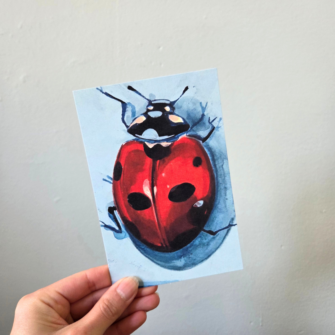 A hand holding an art print postcard featuring a ladybug.