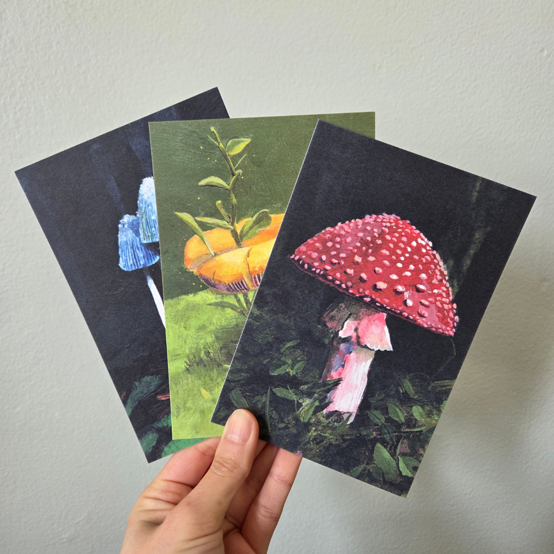 A hand holding three art print postcard featuring mushrooms.