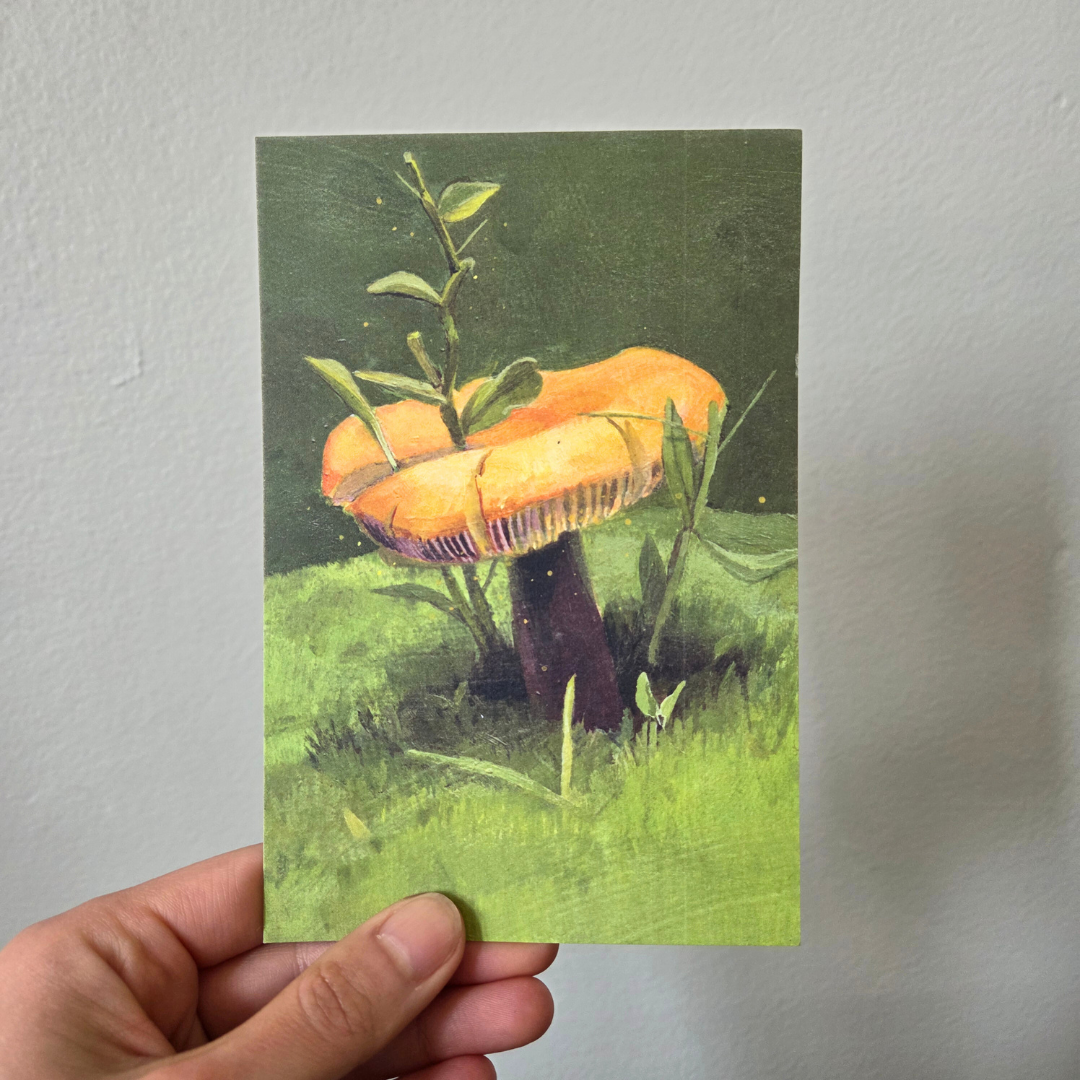 A hand holding an art print postcard featuring a golden wax cap mushroom.