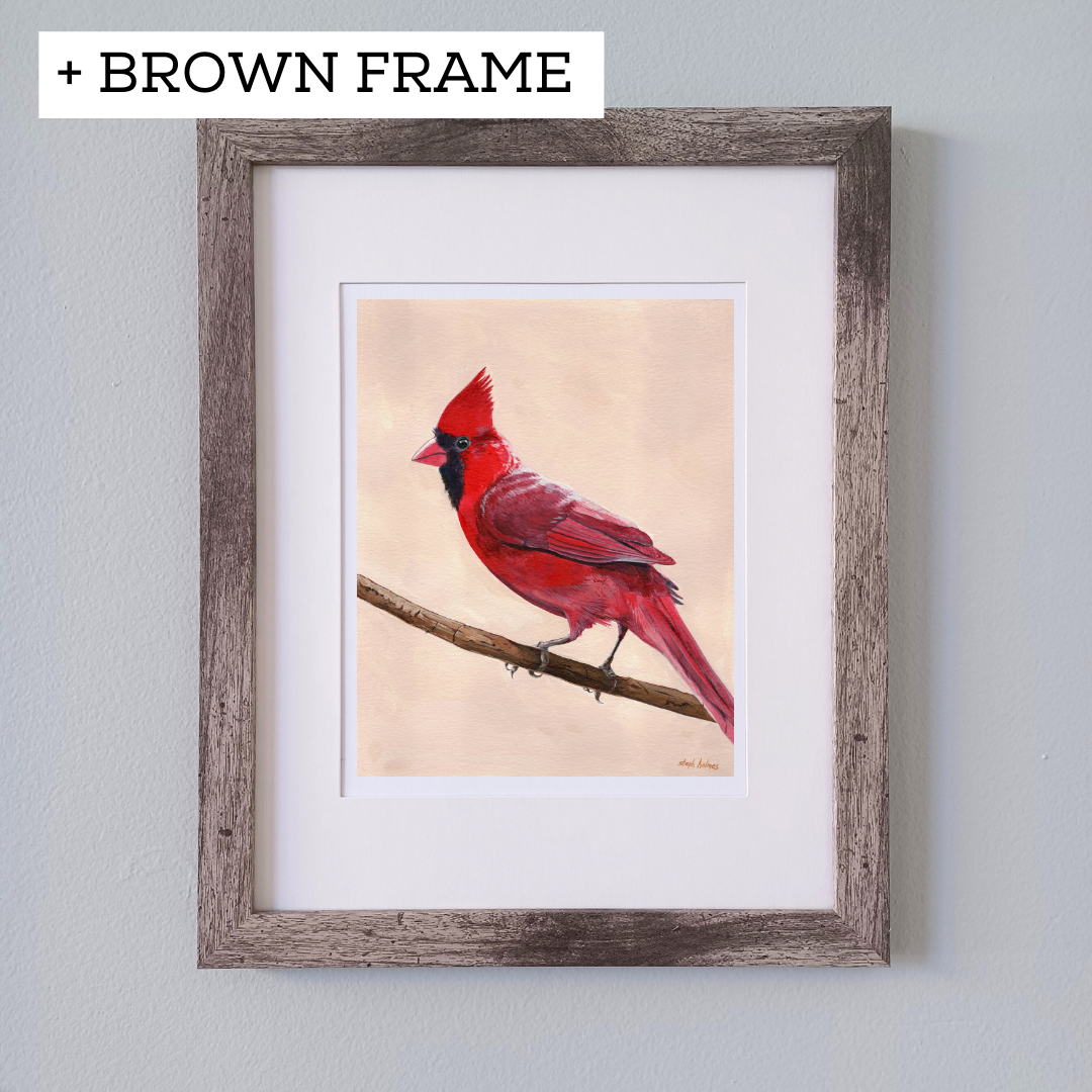 An art print featuring a bright red northern cardinal bird in a brown frame on a white wall.
