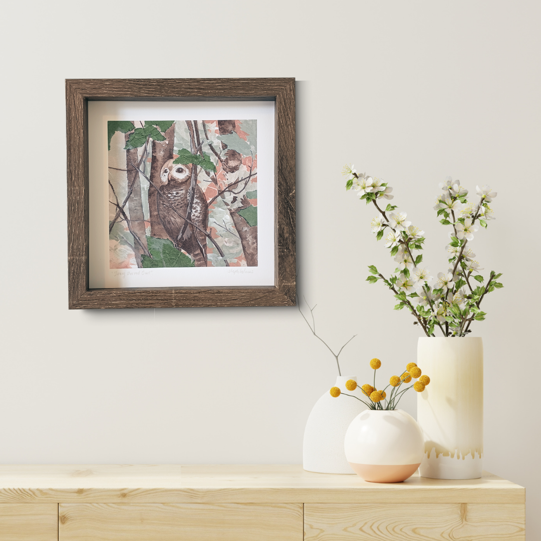 A photo of a framed Young Barred Owl print above a table with vases and flowers.