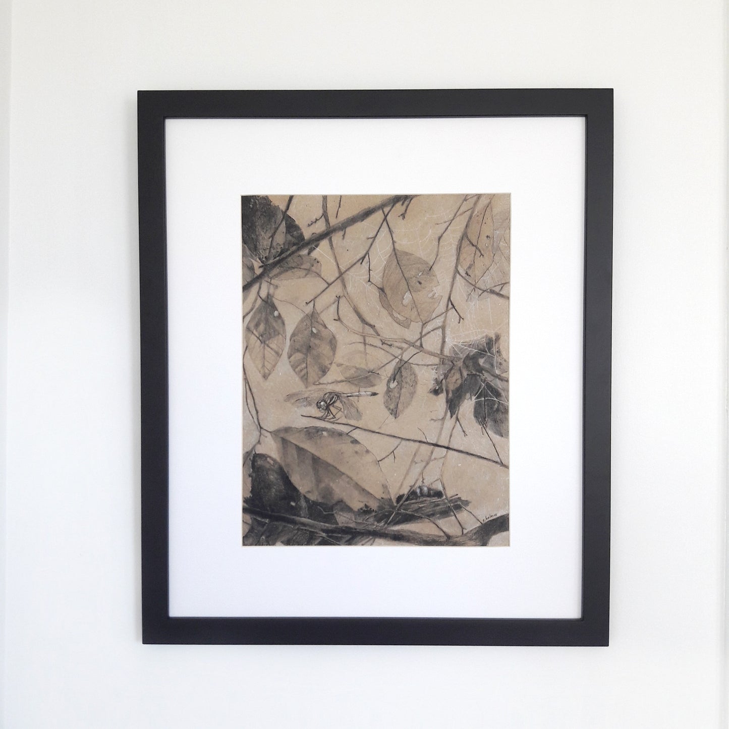 A photograph of a charcoal drawing in a black frame on a white wall.
