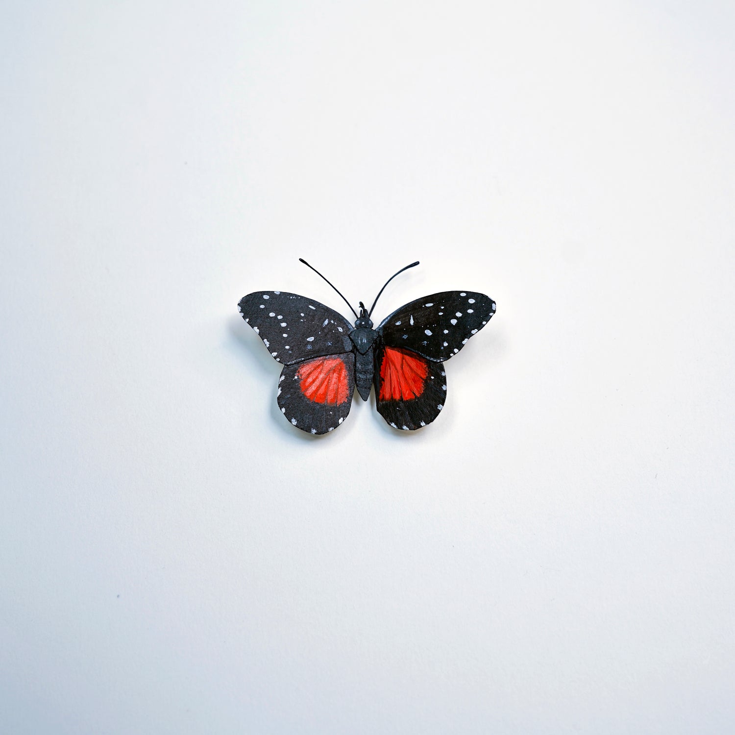 A butterfly art sculpture with black wings speckled with white dots and vibrant red patches on the hindwings, centered on a plain white background.