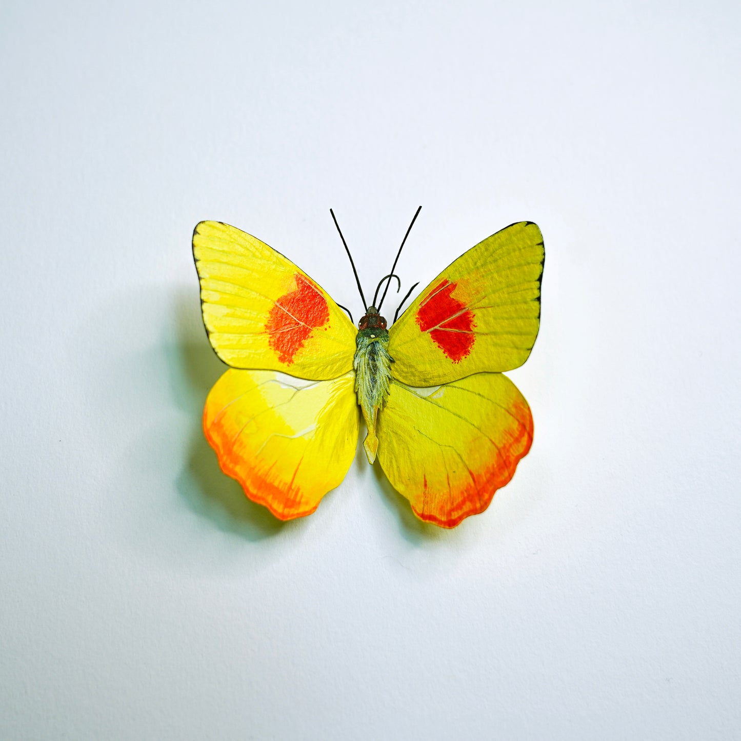A butterfly art sculpture with bright yellow wings featuring red spots and orange edging, displayed against a plain white background.