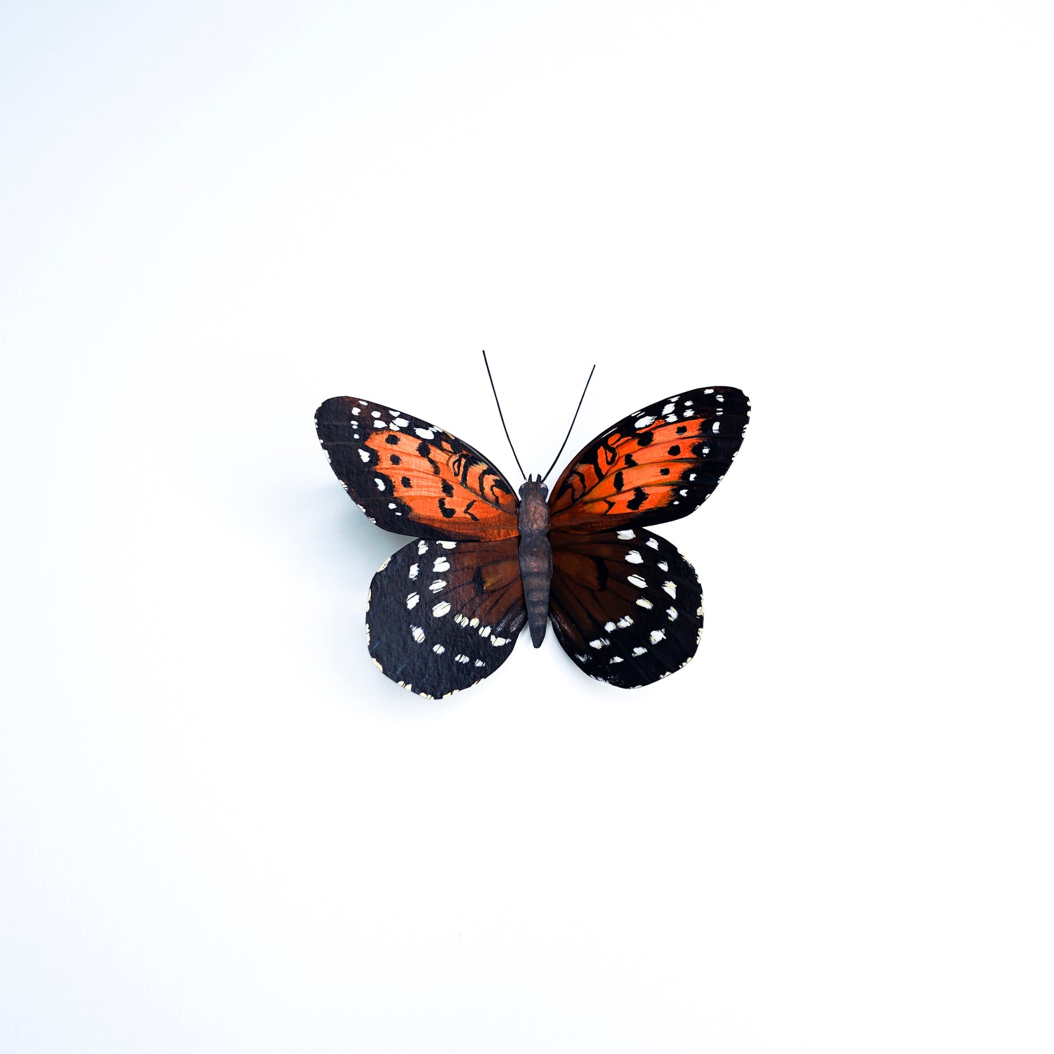 A butterfly art sculpture with bright orange wings and black borders decorated with small white spots, centered on a plain white background.