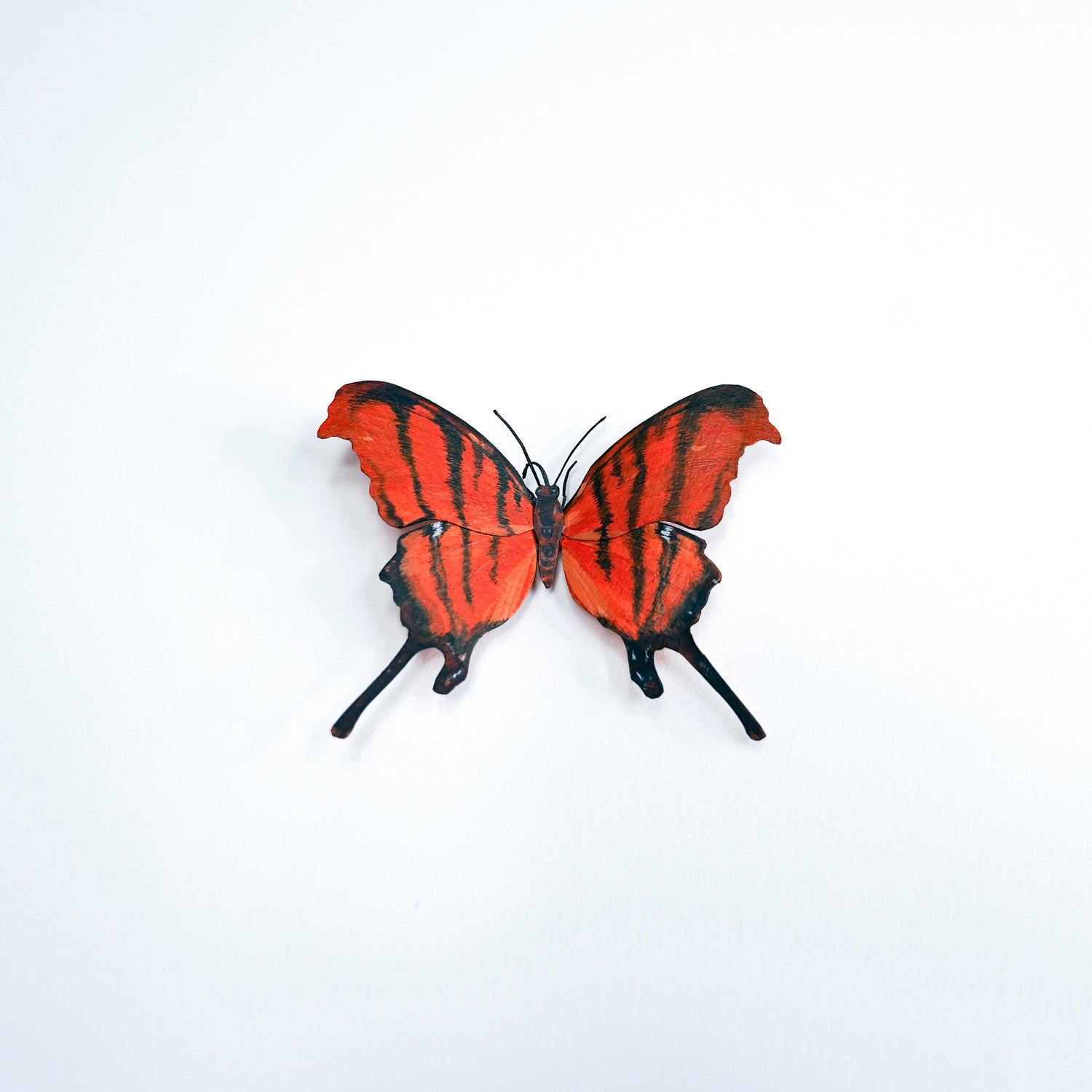A butterfly art sculpture with bright red-orange wings and bold black stripes, displayed against a plain white background.