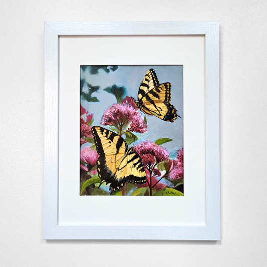 A framed painting featuring two yellow and black swallowtail butterflies perched among pink flowers against a light blue sky, presented in a white frame with a white mat on a light gray wall.