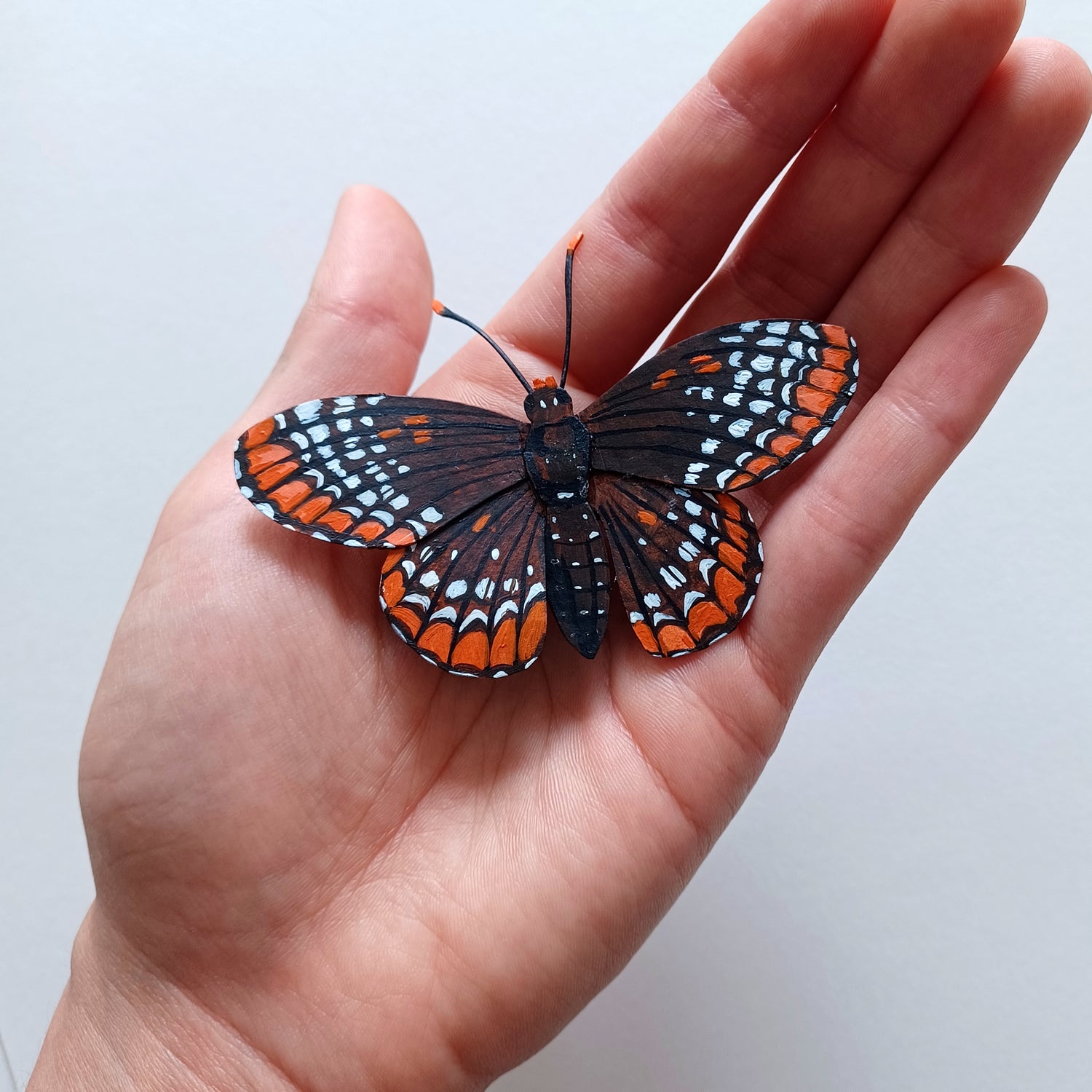 A baltimore checkerspot butterfly sculpture by artist Steph Holmes in a hand for scale.