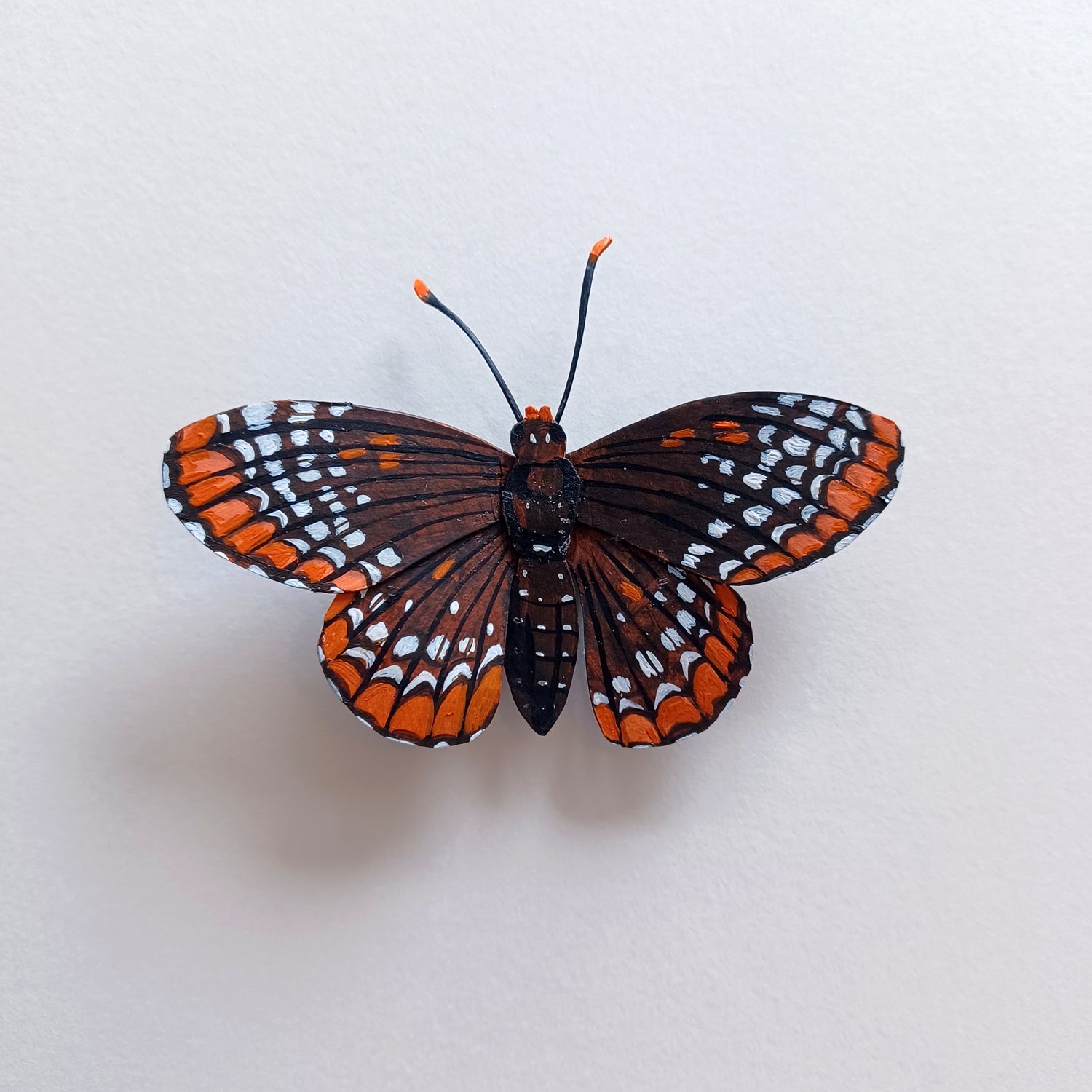 A baltimore checkerspot butterfly sculpture by artist Steph Holmes on a white table.