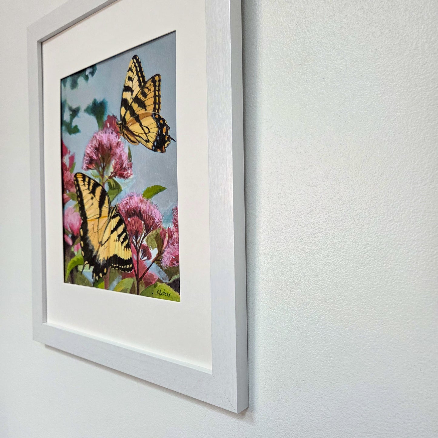 Framed wall art featuring two yellow-and-black swallowtail butterflies among pink flowers, mounted on a white wall.