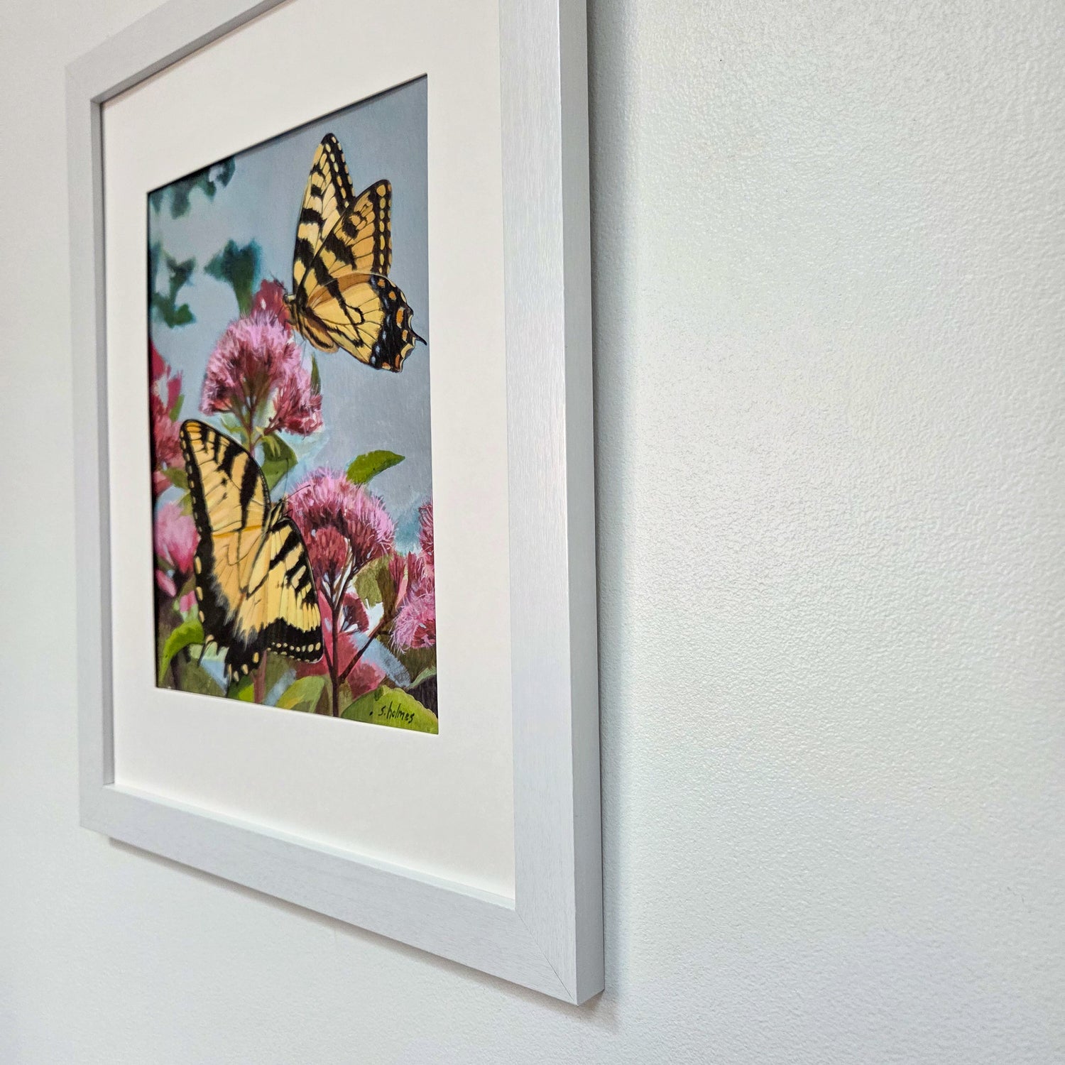 Framed wall art featuring two yellow-and-black swallowtail butterflies among pink flowers, mounted on a white wall.