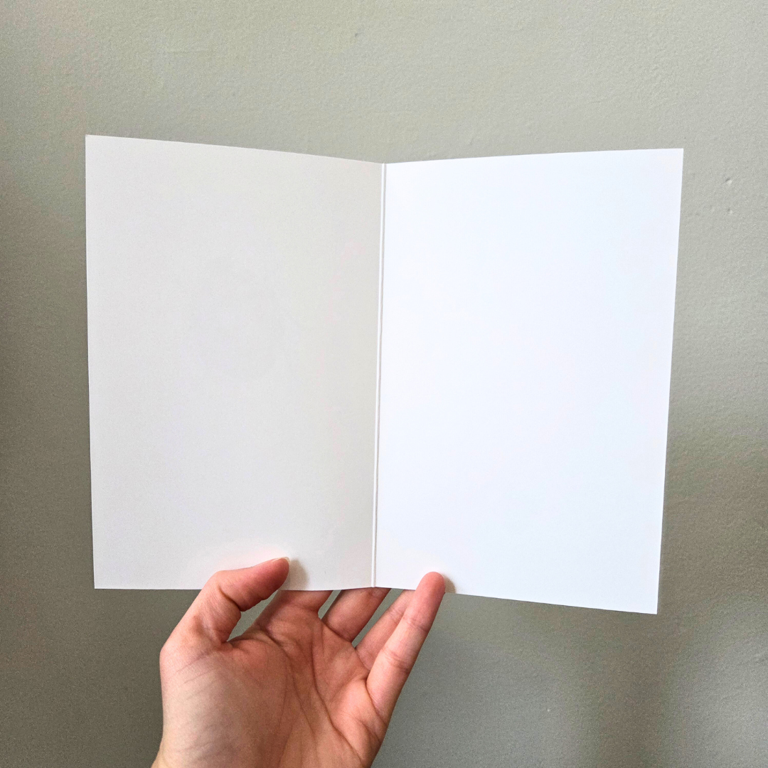 A hand holding an open, blank greeting card.