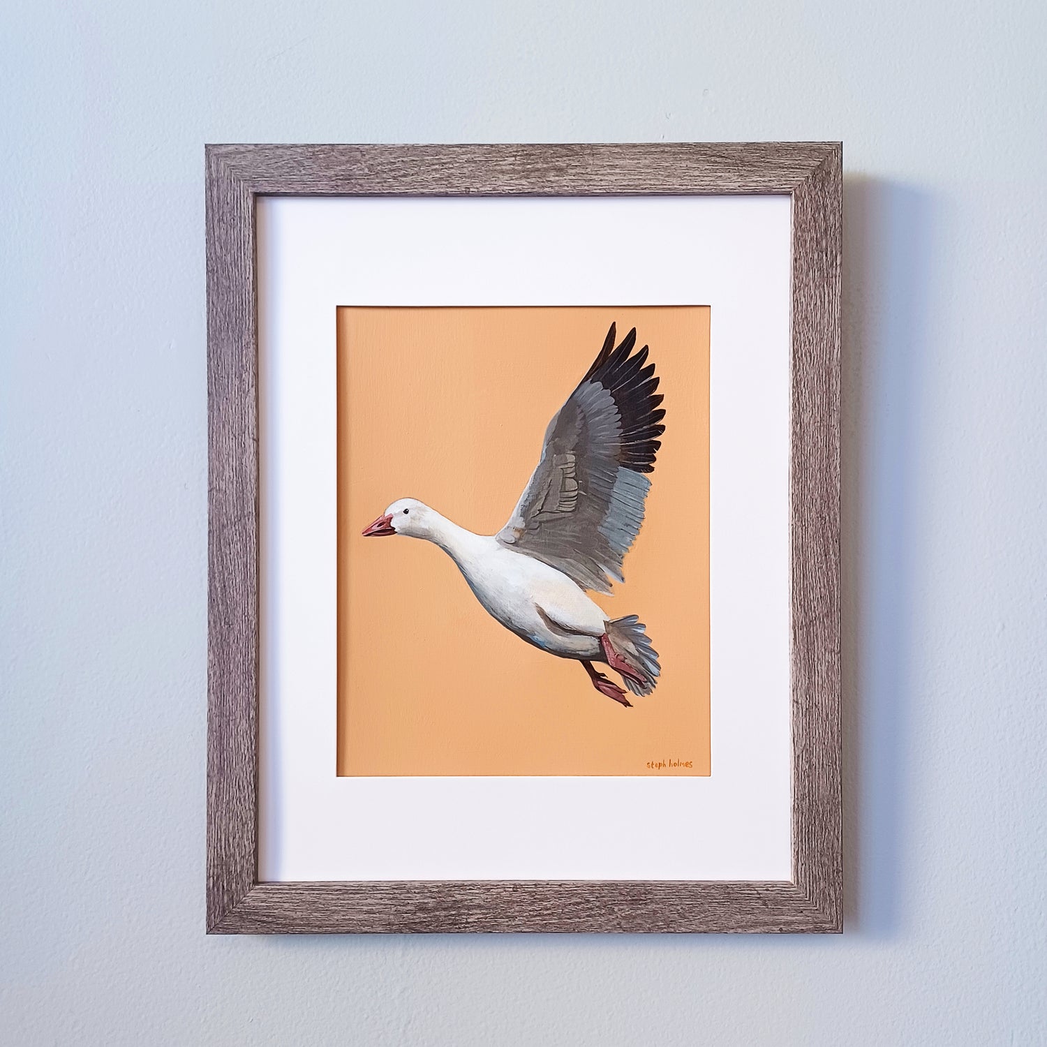 This is a painting of a snow goose framed in a brown frame on a gray wall.