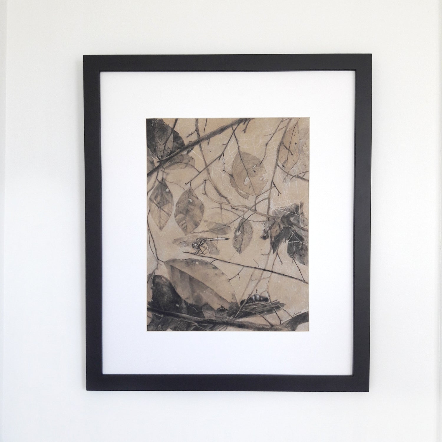 A photograph of a charcoal drawing in a black frame on a white wall.